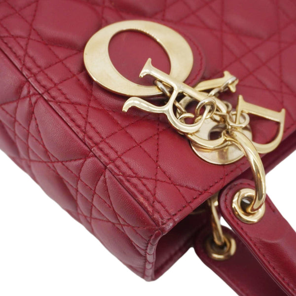 Close-up of gold Dior charm on Lady Dior Medium Red Leather Bag