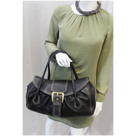 Woman is holding Celine black leather buckle satchel bag